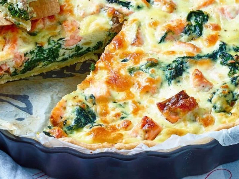 Angeschnittene Lachs-Spinat-Quiche in einer runden Form auf einem Tisch.