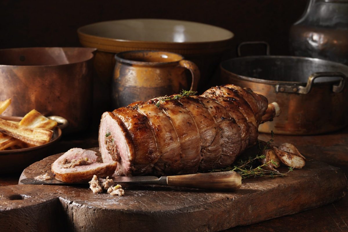 Braten auf Holzbrett mit Töpfen im Hintergrund