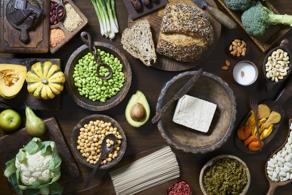 eine Auswahl an ballaststoffreichen Lebensmittel wie Brot, Kichererbsen, Blumenkohl, Brokkoli, Bohnen und mehr in der Draufsicht.