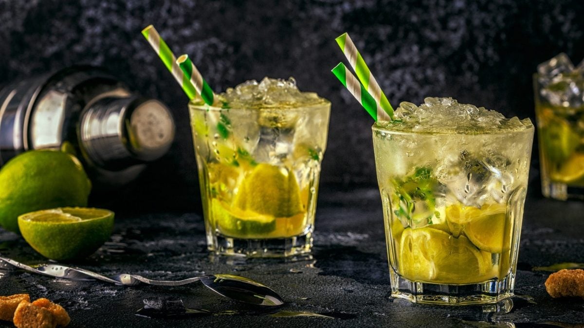 Caipirinha-Bowle in zwei Gläsern mit Strohalmen, Eis und Limetten.