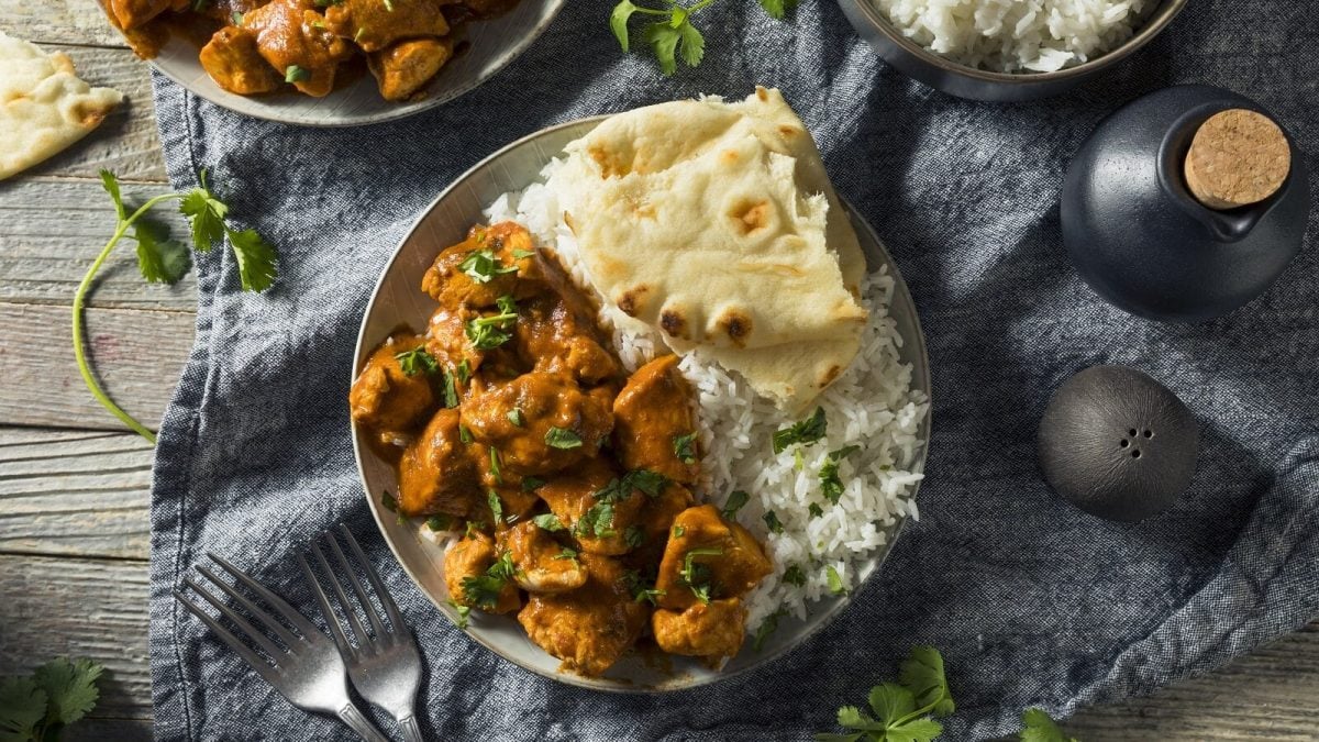 Schale mit Chicken Tikka und Nuss-Pilaw mit Naan-Brot auf einer Tischdecke von oben