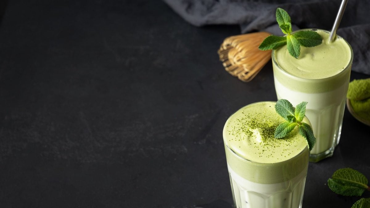 zwei Gläser Dalgona Matcha mit frischer Minze auf einem schwarzen Tisch.