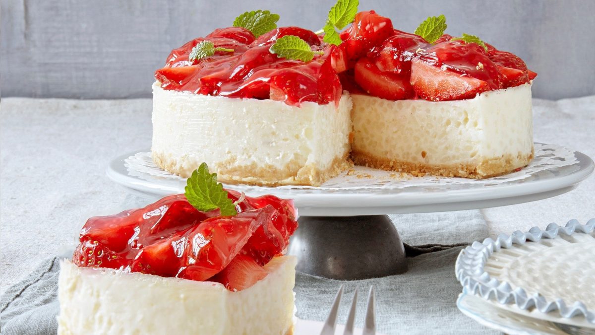 Aufgeschnittene Erdbeertorte mit Milchreis auf einem hellen Tisch mit einer grauen Tischdecke vor einem grauen Hintergrund.