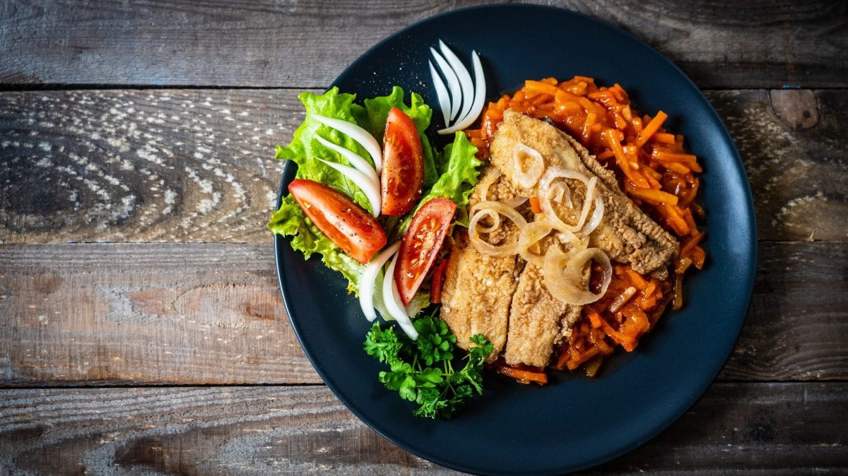 Gebratenes Fischfilet mit Tomatensauce : ein Teller mit Tomaten-Möhren-Soße, Fisch und Salat auf einem Holztisch.