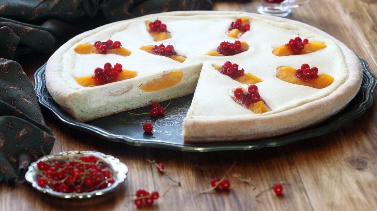 Tarte mit griechischem Joghurt und Früchten auf schwarzem Teller, daneben Johannisbeeren