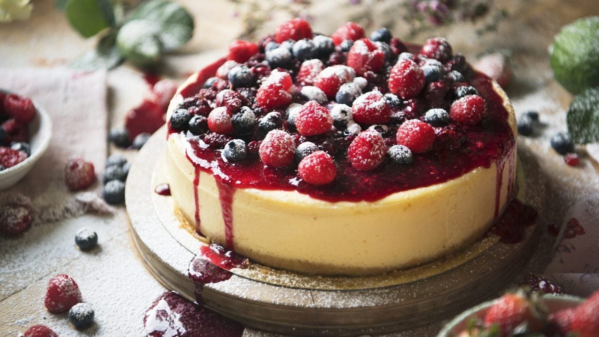 Himbeer-Schmand-Torte ohne Backen mit Himbeeren, Blaubeeren und roter Soße dekoriert.