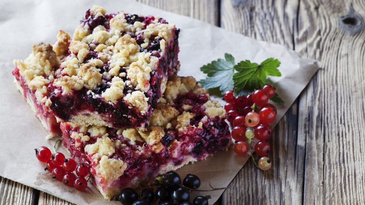 Streuselkuchen mit roten und schwarzen Johannisbeeren auf einem Stück Papper auf einem unbehandelten Holztisch.