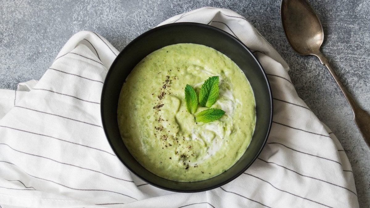 Kalte Gurkensuppe mit Minzblättern garniert und in einer schwarzen Schüssel serviert, von oben auf grauem Hintergrund