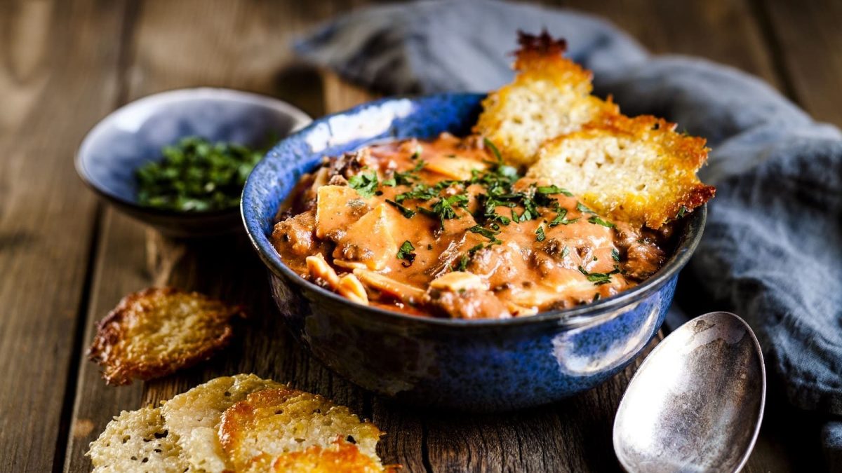 Eine Schüssel mit Lasagne-Suppe, garniert mit Basilikum und Parmesan Crisps auf einem Holztisch