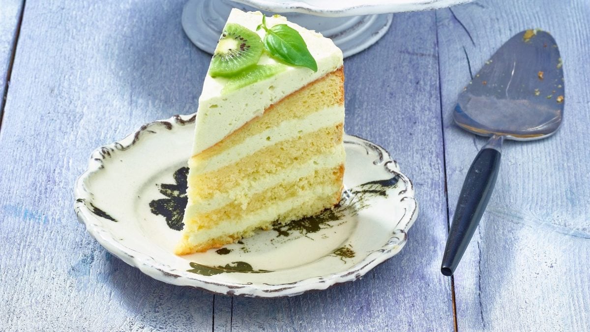 Limetten-Basilikum-Torte mit einem Tortenheber auf blauem Holz-Untergrund