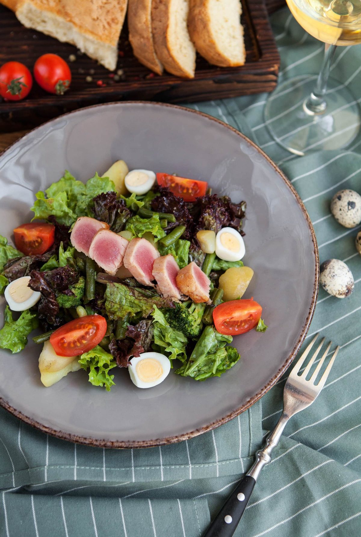 Nizzasalat mit frischem Fisch, daneben Gabel und ein Weißweiglas