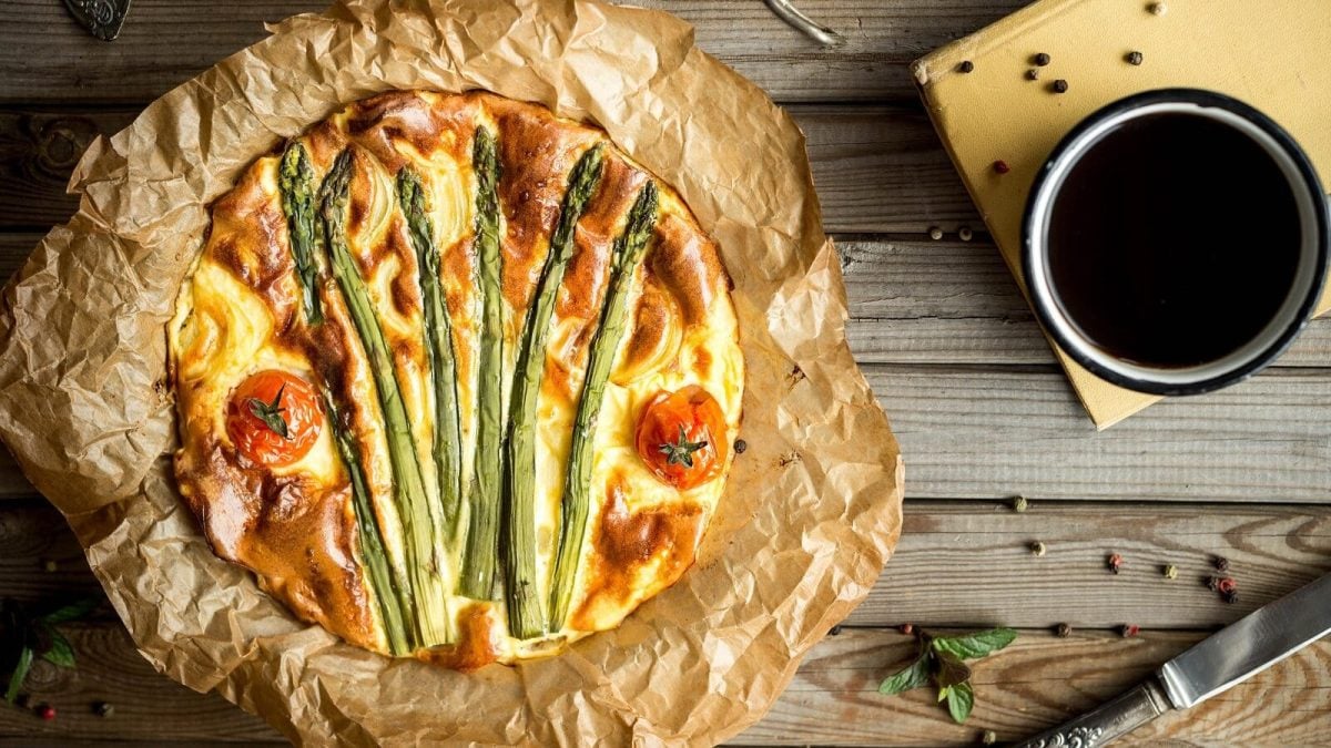 Eine frischgebackene Spargelquiche mit Kirschtomaten von oben auf Holzhintergrund