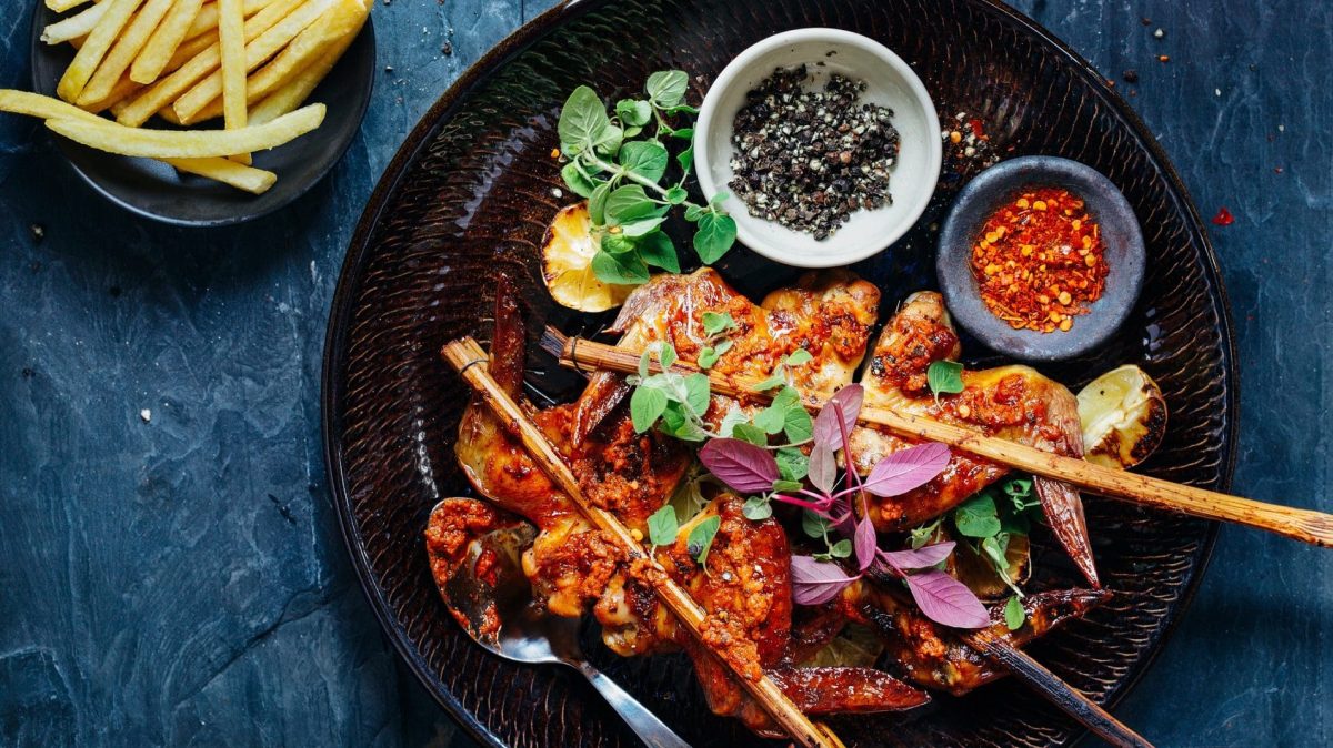 Thailändisches Hähnchen mit Teriyakisoße: ein Teller mit Hähnchenspießen, Gemüse und einer Schale mit Pfeffer- und Chilikörner. Daneben eine Schüssel Pommes.