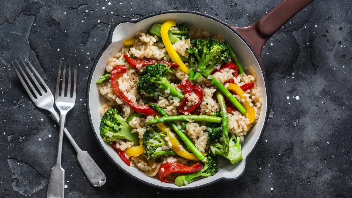 Vegetarische Reispfanne mit Paprika und Brokkoli, daneben zwei Gabeln auf dunklem Untergrund.