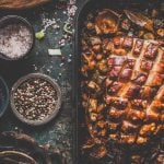 Ein Braten mit ziselierter Kruste liegt auf einer Schieferplatte mit allerlei Gewürzen drumherum