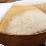 Eine Kugel Hefeteig wird gehen gelassen: Der Teig befindet sich in einer Keramik-Schüssel und ist zur Hälfte mit einem Tuch bedeckt.