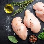 Rohes Hähnchenfleisch für eine Farce von oben auf einem schwarzen Tisch mit frischen Pfefferkörnern, Basilikum, Salz, Thymian und einem Glas Öl.