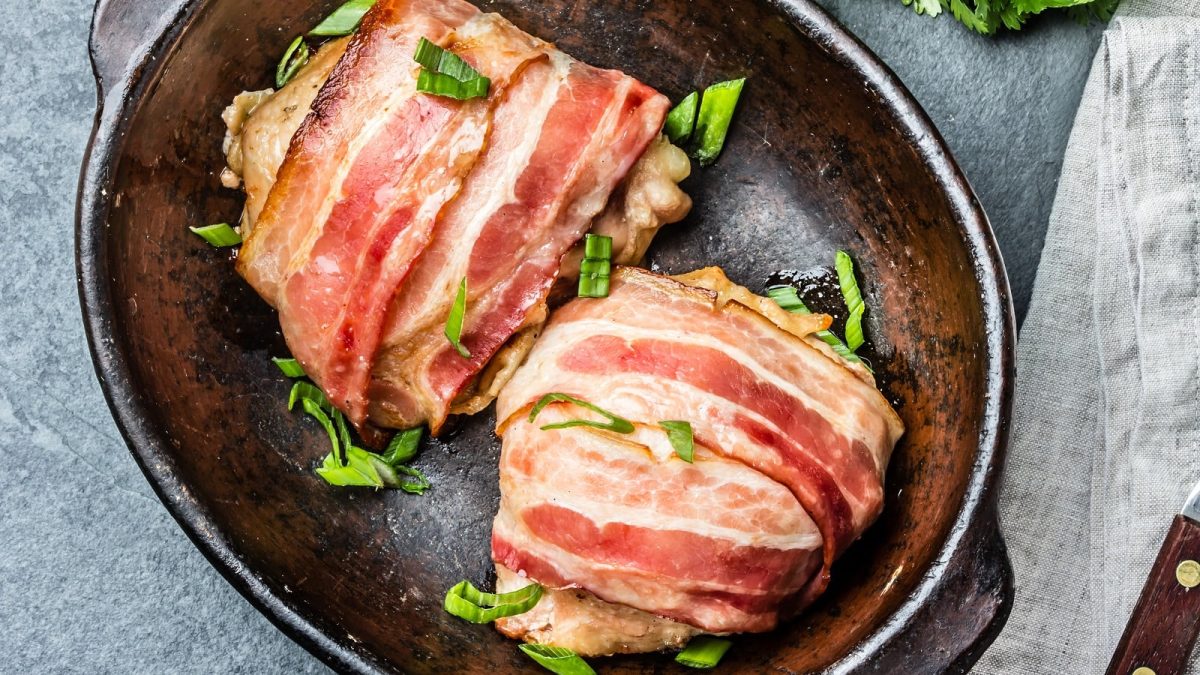 Fleisch bardieren: Zwei bardierte Hühnerfilets in Speck eingewickelt und mit Kräutern besträut in einer Schale, von oben.