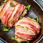 Fleisch bardieren: Zwei bardierte Hühnerfilets in Speck eingewickelt und mit Kräutern besträut in einer Schale, von oben.
