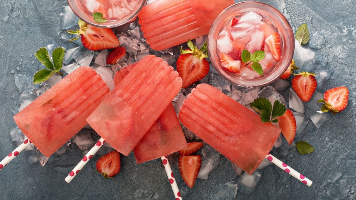 Erdbeer-Margarita Pop-Sicles auf grauer Unterlage, daneben Erdbeeren
