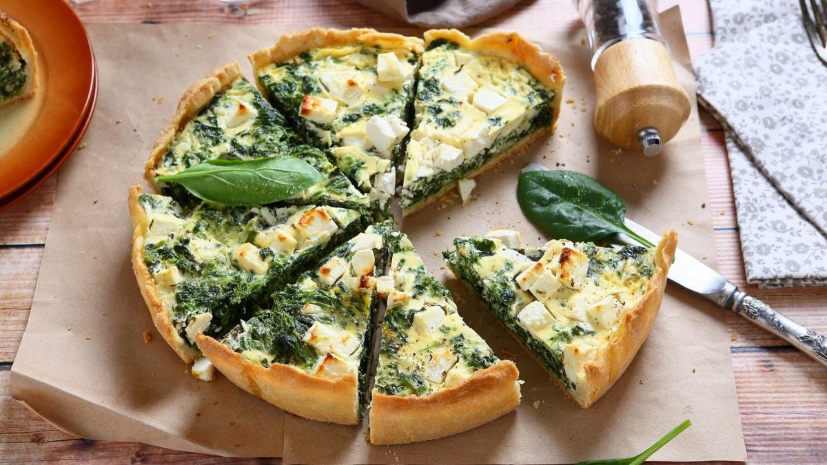 Spinat-Quiche mit Ziegenkäse und Rosinen auf Backpapier, daneben ein umgekippter Pfefferstreuer und ein Messer.