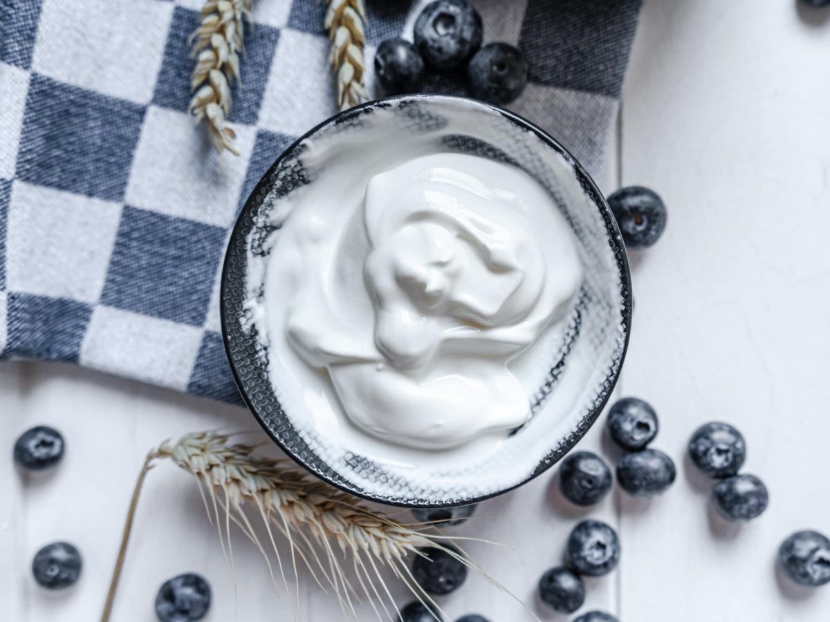 Warum rahmt sahne auf: eine Schale mit Schlagsahne, drumherum liegen Blaubeeren, Getreide und ein Geschirrtuch