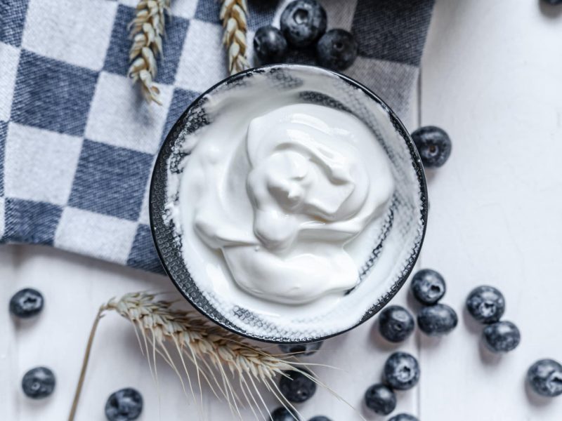 Warum rahmt sahne auf: eine Schale mit Schlagsahne, drumherum liegen Blaubeeren, Getreide und ein Geschirrtuch