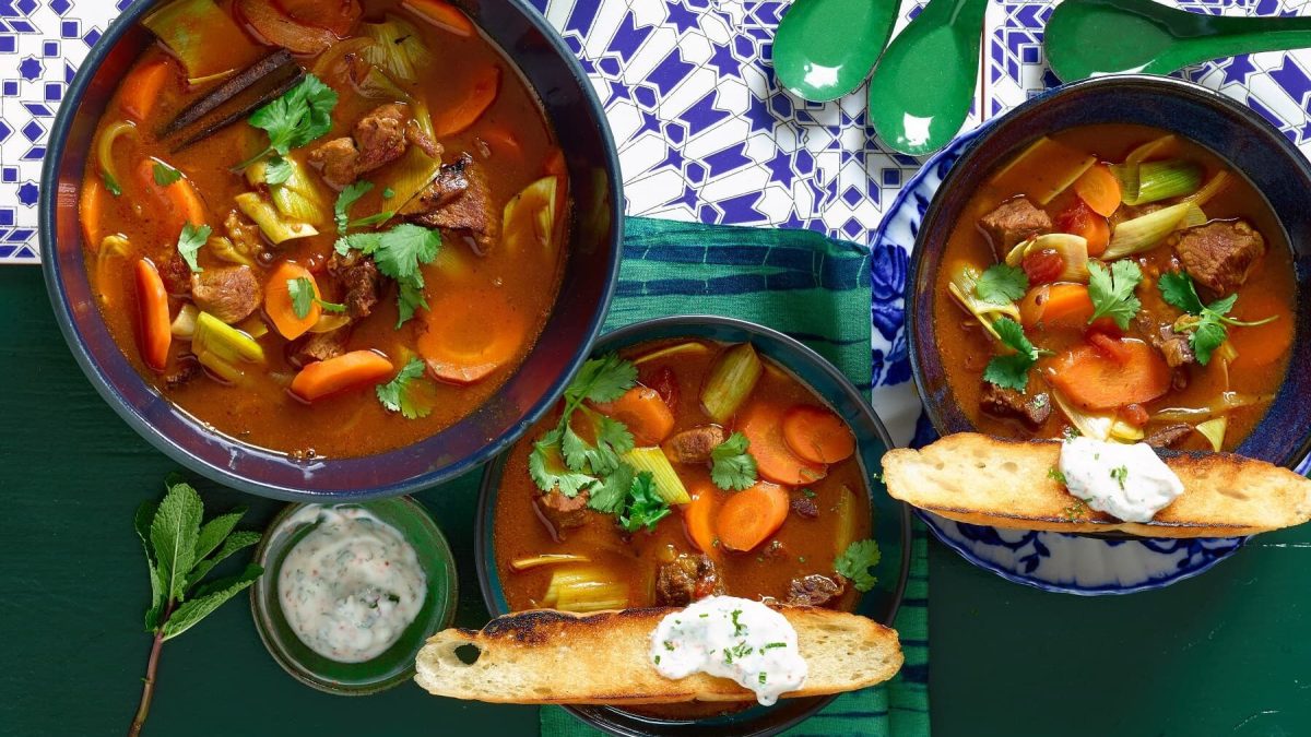 Arabische Gulaschsuppe in drei verschiedenen Tellern mit Brot und Dip auf einem Fliesentisch mit Löffeln und einem Brotkorb.