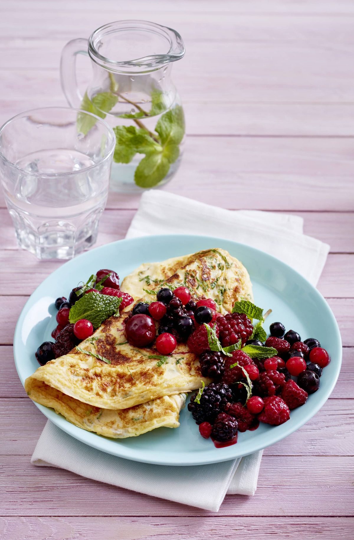 Pfannkuchen mit Minze auf blauem Teller mit Beeren