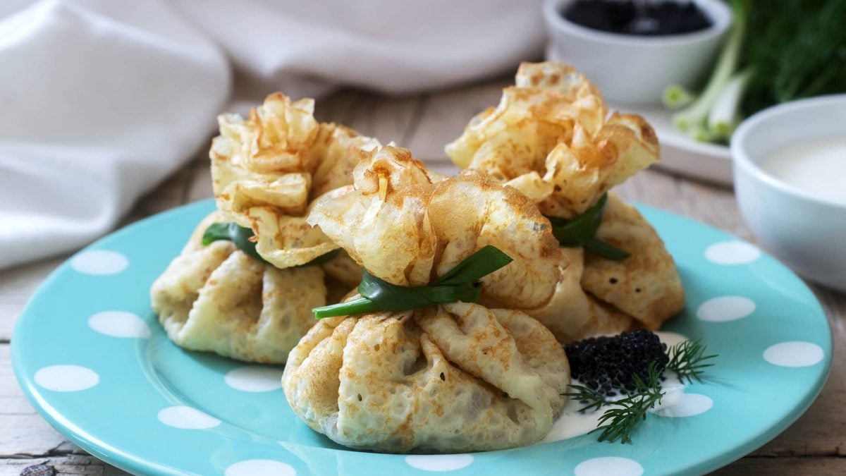 Gefüllte Pfannkuchen mit Spinat und Frischkäse auf einem blauen Teller, daneben eine Schale mit Kaviar.