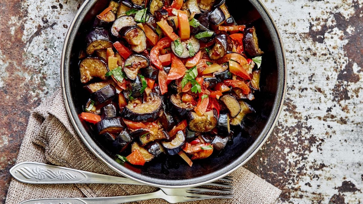 Paprika-Auberginen-Pfanne und einer dunklen Schale. Daneben Besteck.