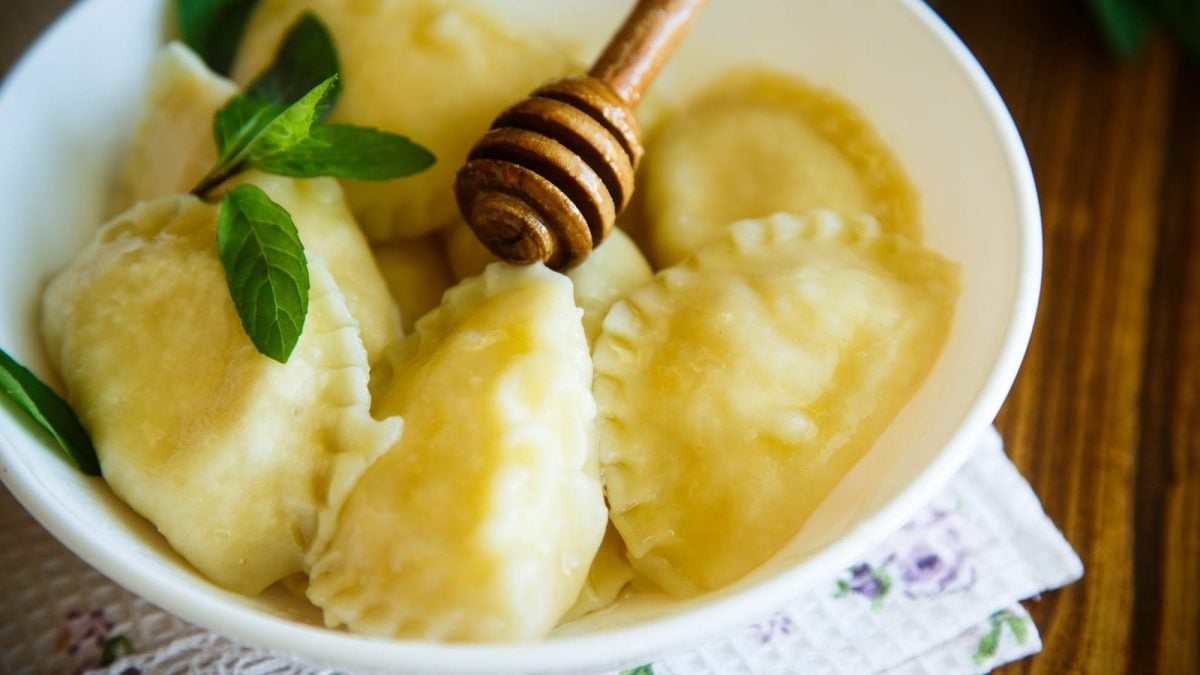 Eine weiße Schüssel gefüllt mit mehreren Ricotta Calcioni, die mit Honig glasiert und mit Minze garniert sind.