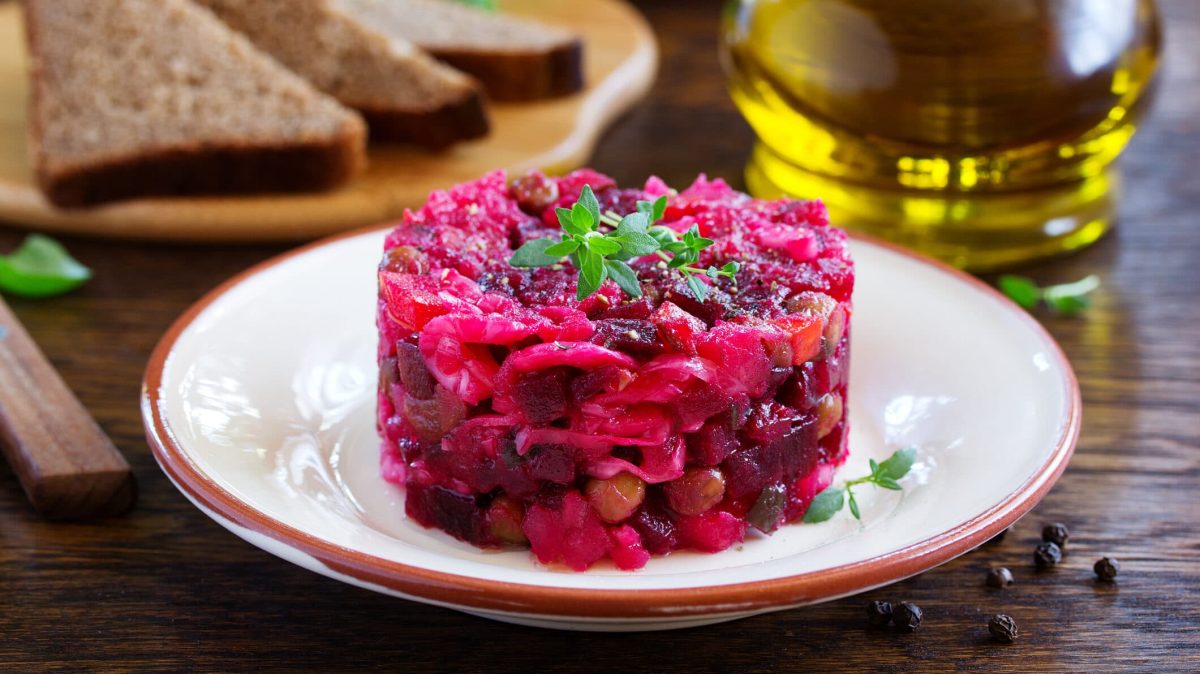 ein Teller mit Rote-Bete-Tatar, im Hintergrund unscharf eine Flasche Öl und ein paar Scheiben Toast.