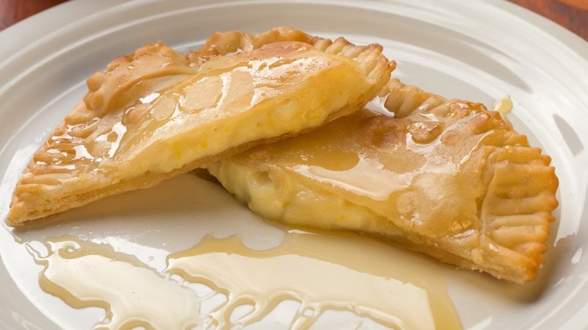 Ein weißer Teller mit zwei Seadas Hälften, die mit Honig glasiert sind und bei denen die Käse-Füllung herausläuft.