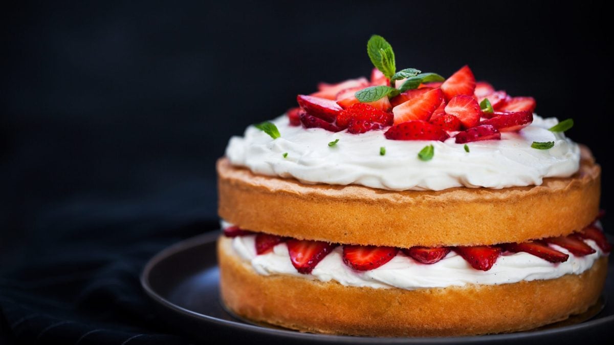 Ein Naked Cake mit Erdbeeren und Sahne auf einem Teller, dekoriert mit frischer Minze.