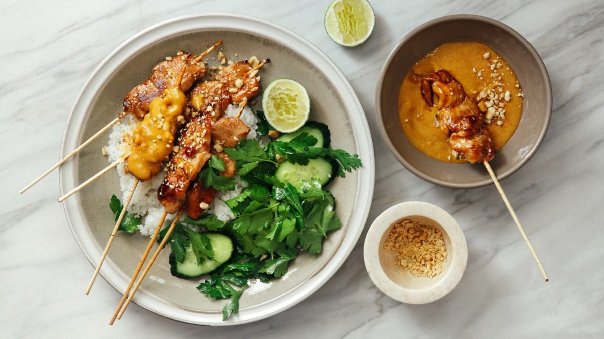 Saté-Spieße mit Erdnusssauce mit Basmati und Koriander. Daneben eine Schale mit Erdnüssen und Erdnussoße.