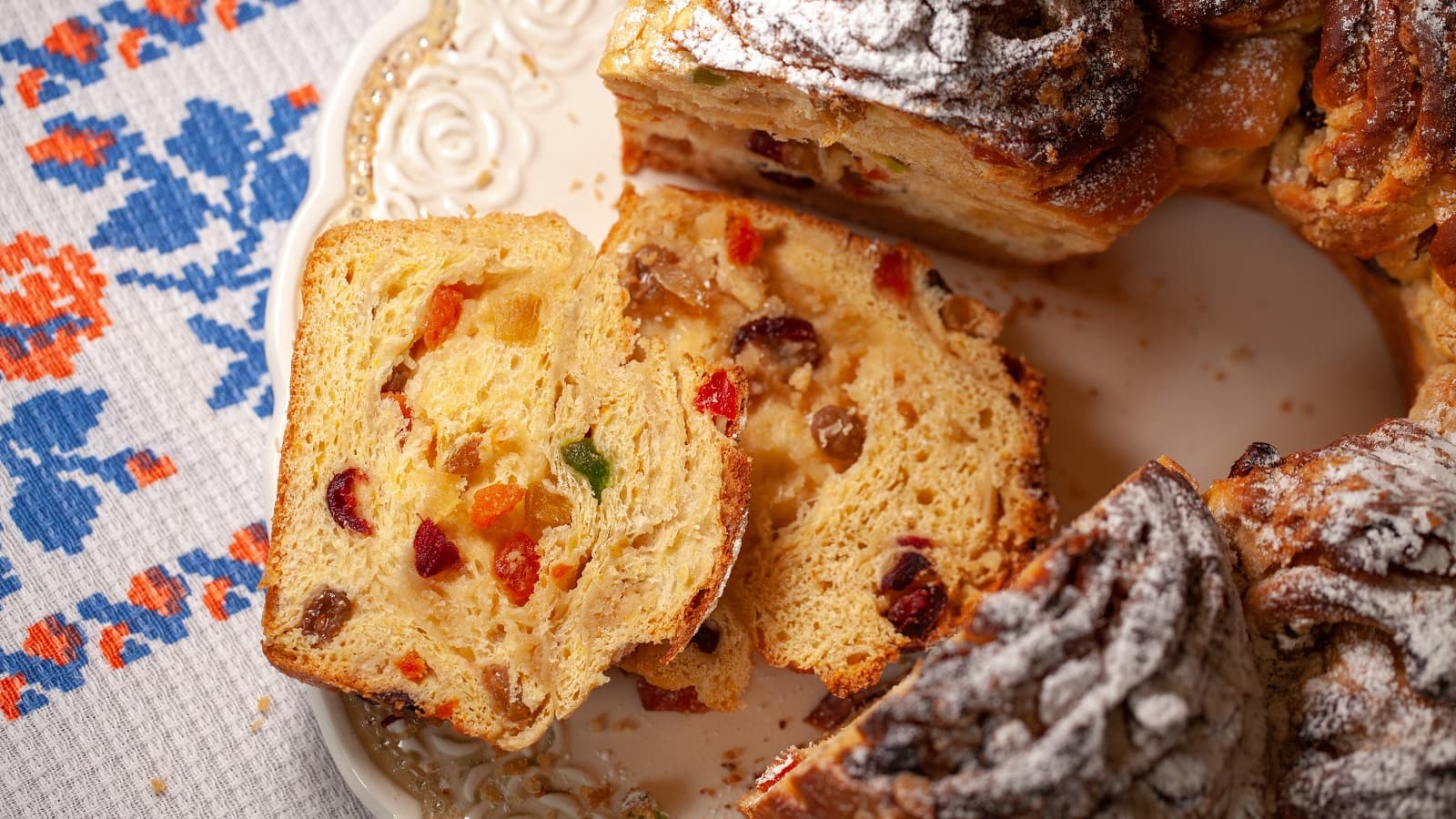 Der traditionelle Kuchen Torcolo aus Umbrien aufgeschnitten mit zwei Stücken, deren Inneres mit kandieren Früchten man sehen kann, auf einem verzierten Teller von oben.