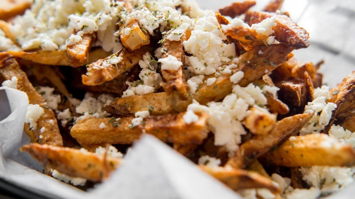Eine Portion Loaded Fries mit Feta liegt in einer mit einer Serviette ausgelegten Metallschüssel. Die Loaded Fries sind mit verschiedenen Gewürzen bestreut.
