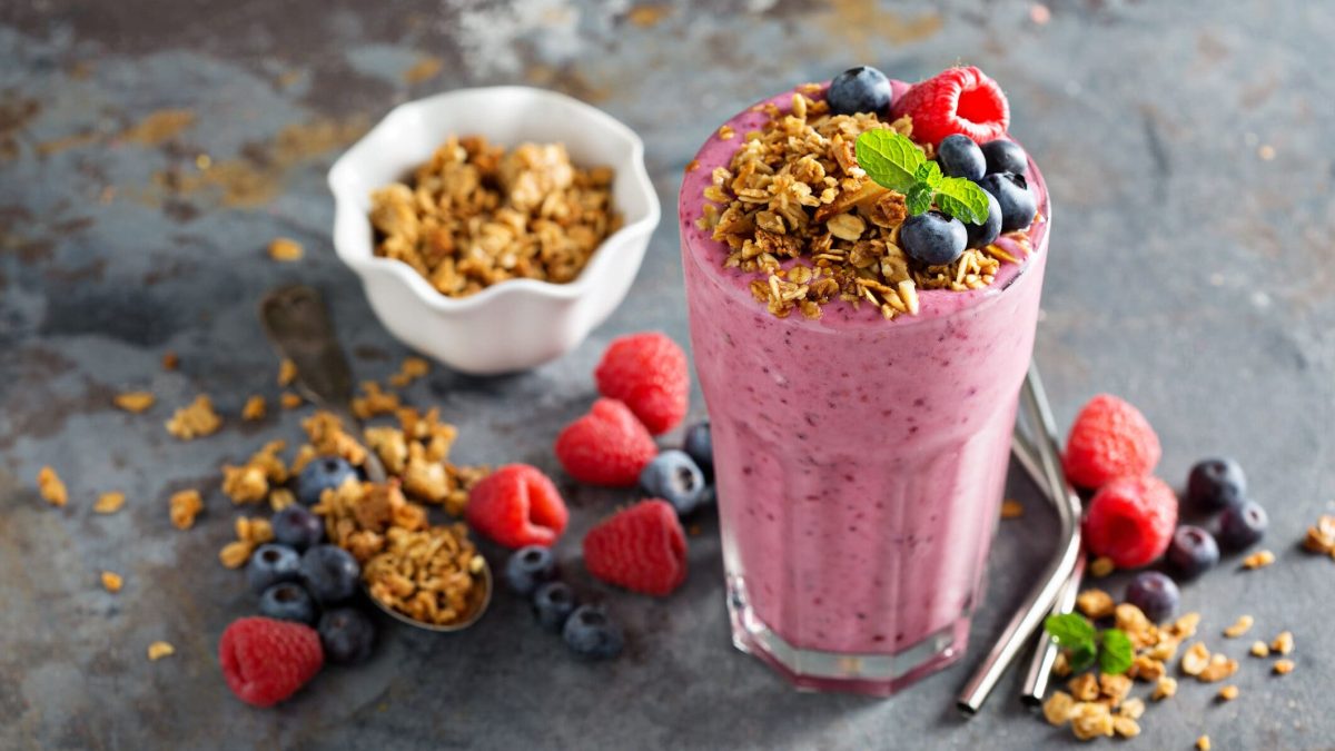 Ein Glas Aronia-Smoothie, dekoriert mit Müsli und frischen Beeren. Drumherum liegen verstreut die Zutaten.