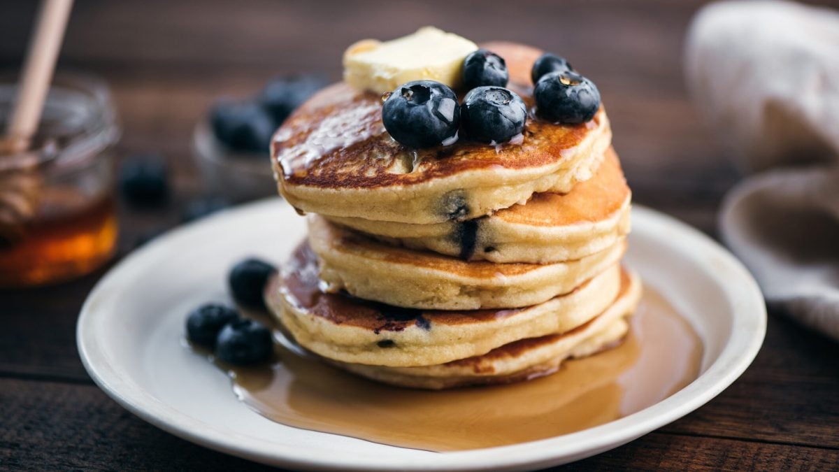 Ein Teller mit einem Stapel glutenfreier Kokos-Pancakes, dazu Blaubeeren und Sirup.