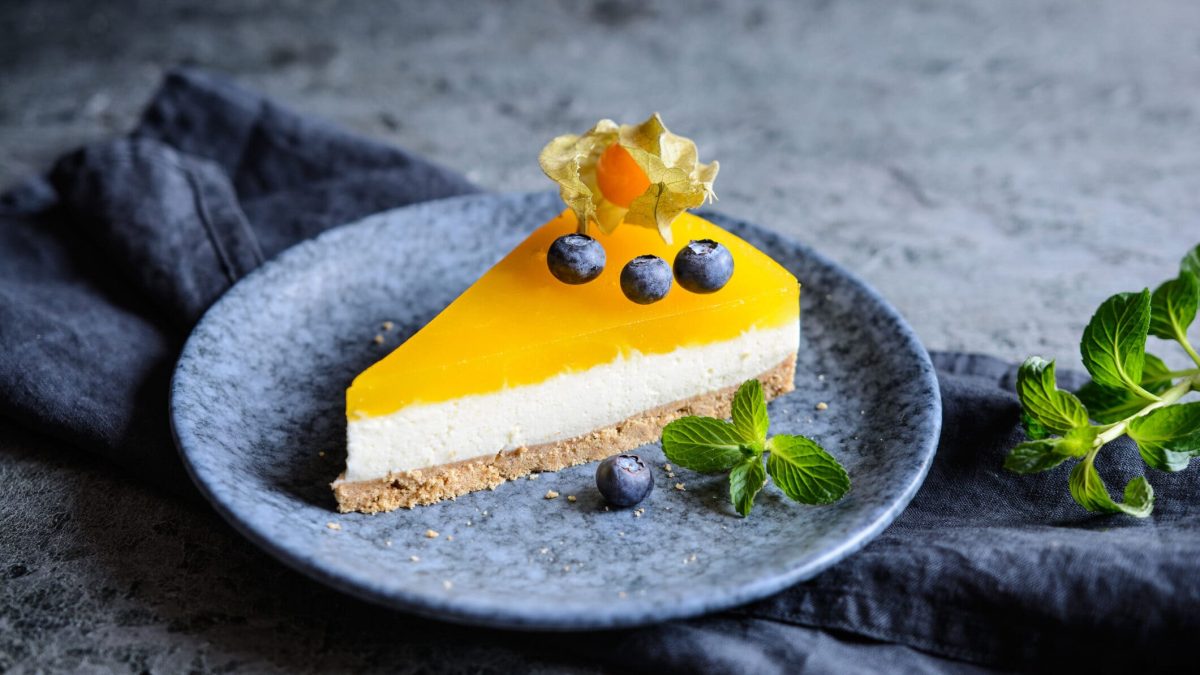 Ein Teller mit einem Stück Mango-Cheesecake, dekoriert mit Blaubeeren und Physalis.