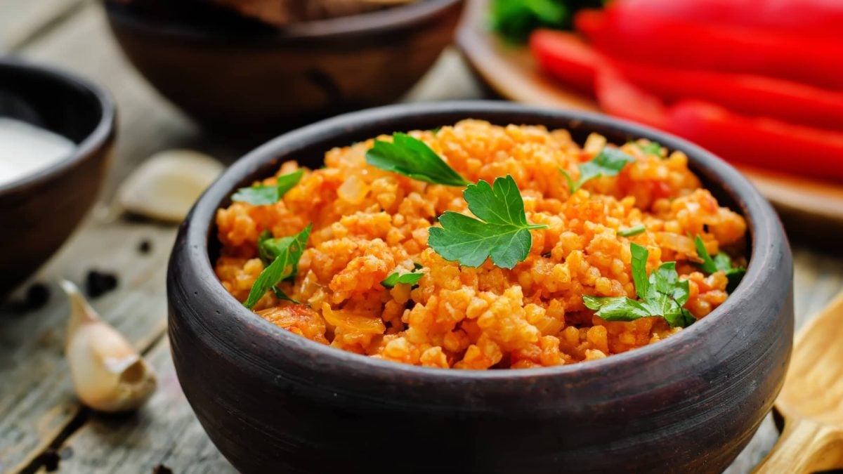 Eine dunkle Schüssel gefüllt mit einer Hirsepfanne mit Möhren und Tomatenmark, darüber ist Peterilie gestreut.