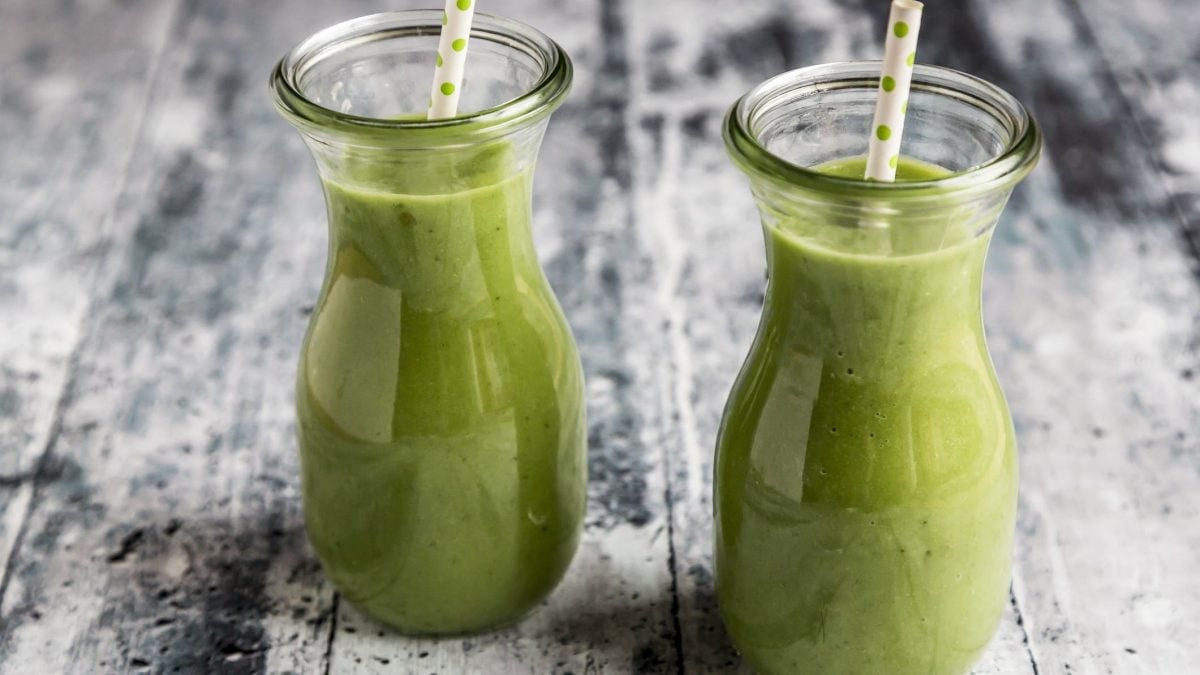 Zwei Gläser mit Smoothie mit Staudensellerie auf einem grauen hölzernen Untergrund.