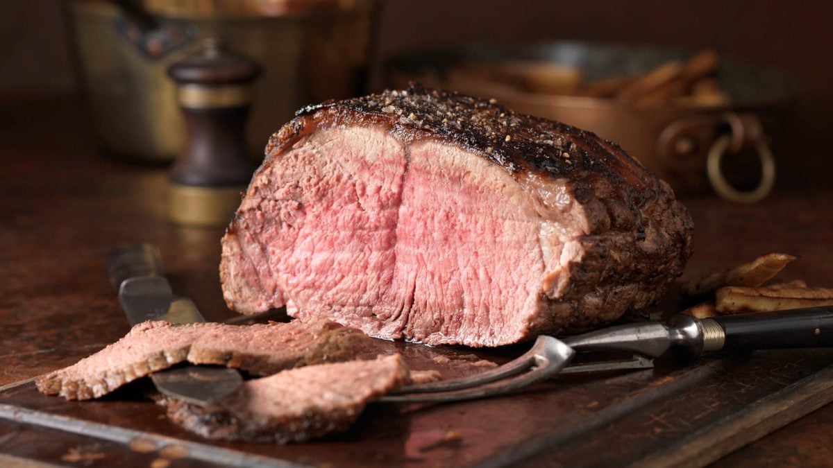 Ein Braten auf einem Holzbrett mit Tranchiermesser und -gabel.
