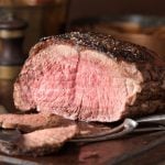Ein Braten auf einem Holzbrett mit Tranchiermesser und -gabel.