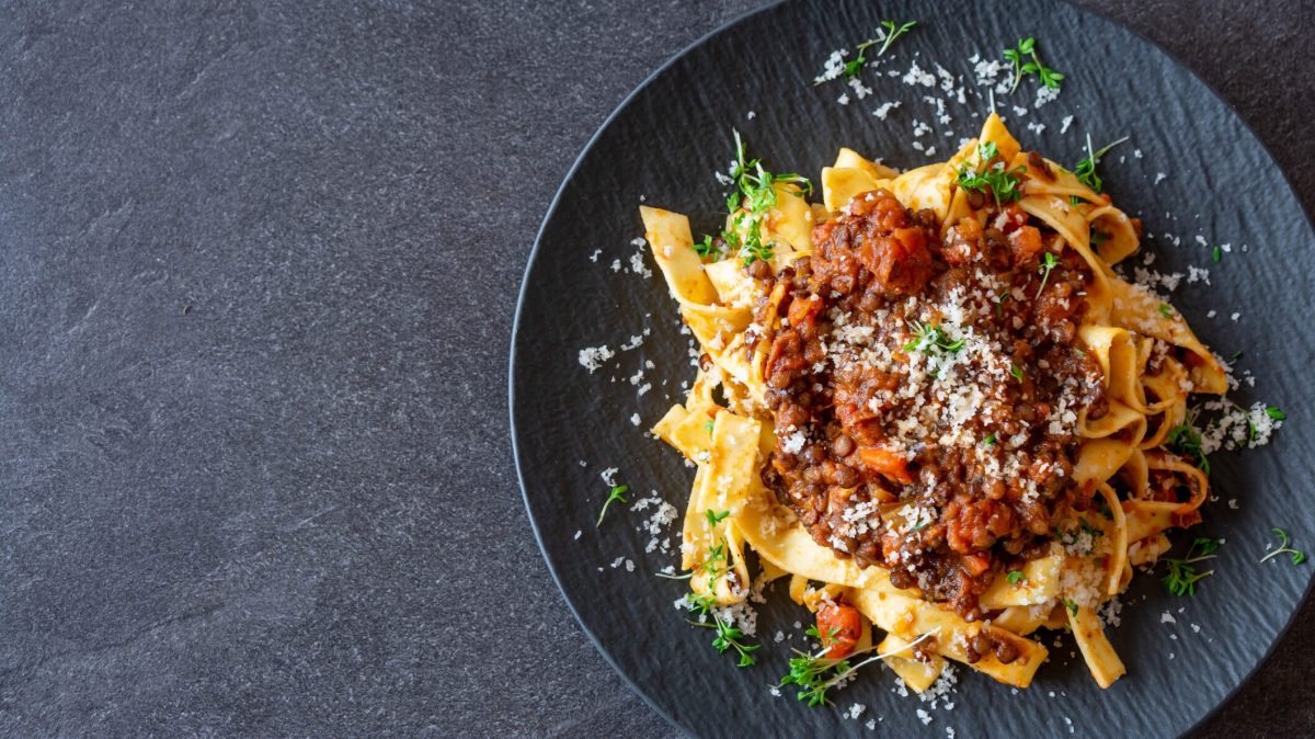 Ein Teller vegetarische Bolognese mit Linsen und Tagliatelle, bestreut mit Parmesan und Kräutern.