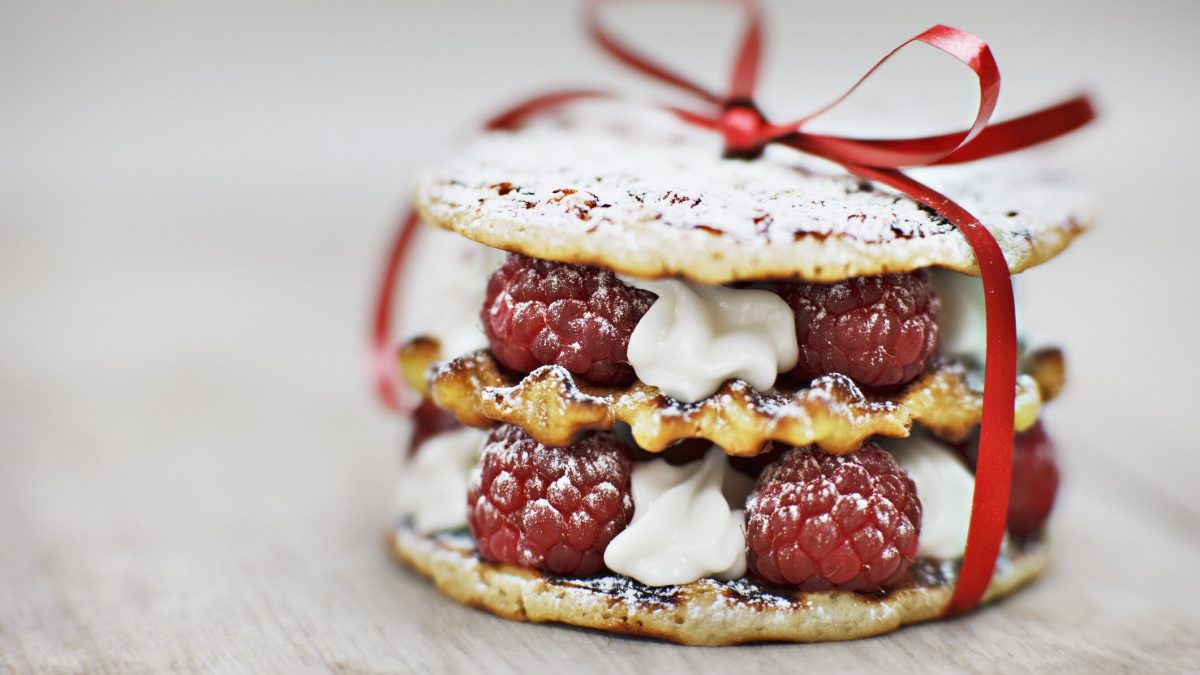 Ein Waffelturm aus belgischen Waffeln gefüllt mit Sahne und Himbeeren und mit einer roten Schleife verziert.