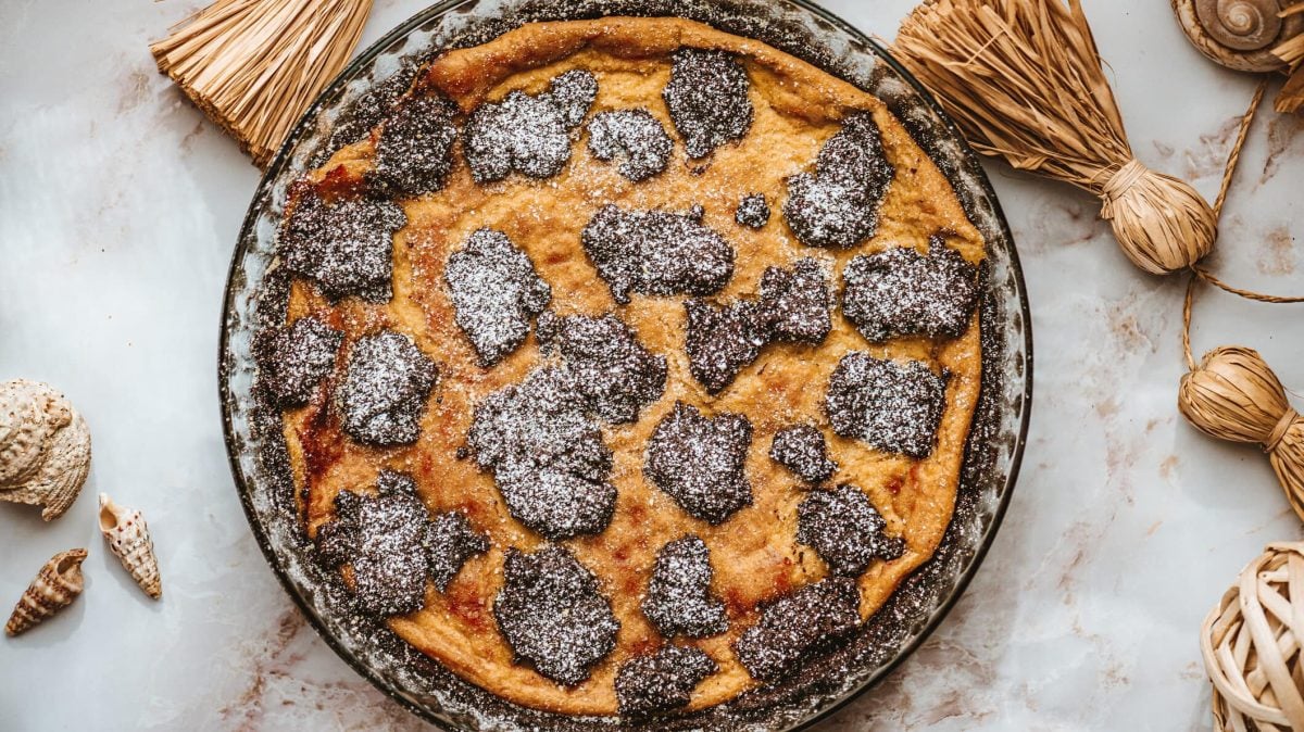 Ein Zupfkuchen mit Mohn und Marzipan in einer Kuchenform, von oben fotografiert. Drumherum etwas Deko aus Stroh und einige Muscheln.