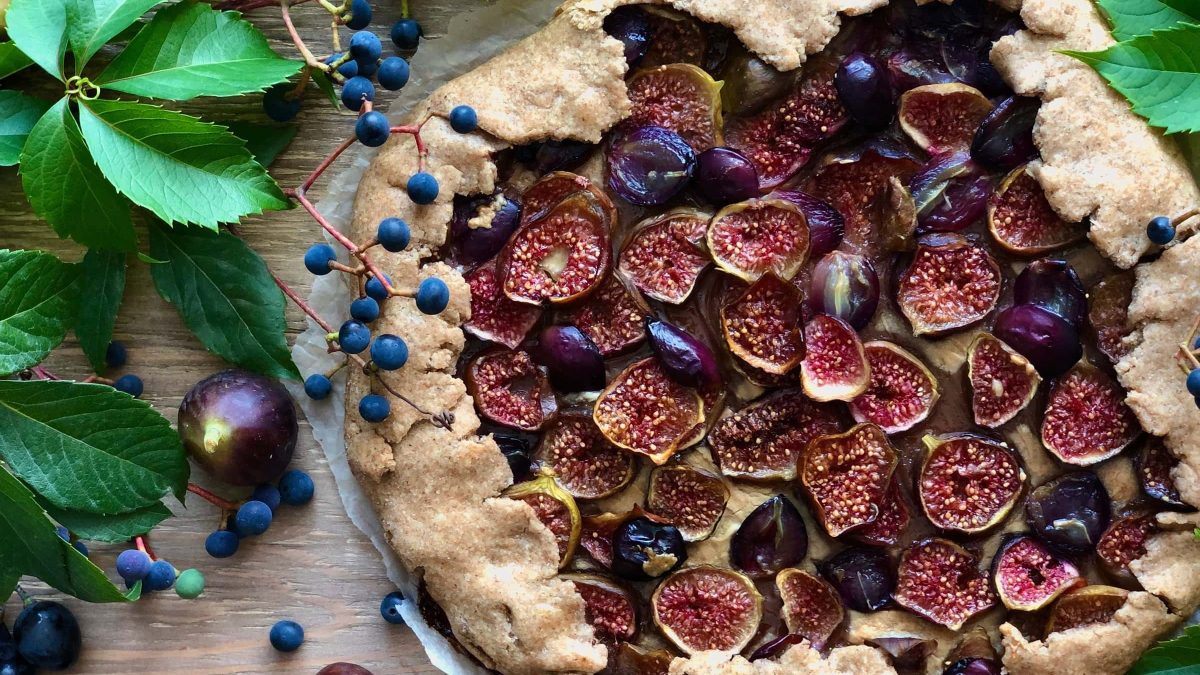 Eine Galette mit Feigen und Weintrauben auf einem Holztisch. Um die Galette herum liegen Blätter, Beeren und einige Feigen.