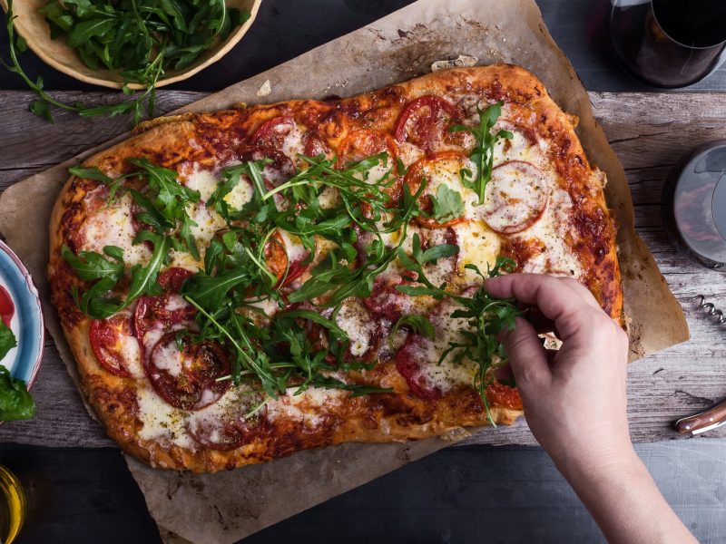 Gebackene Pizza wird mit Rucola belegt